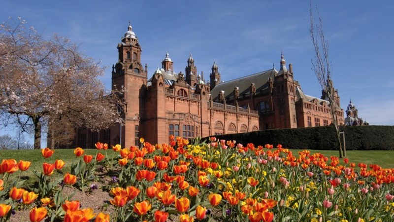 Glasgow's Kelvingrove Art Gallery and Museum on a spring day. There are red and yellow tulips in the foreground, as well as a tree with no leaves.