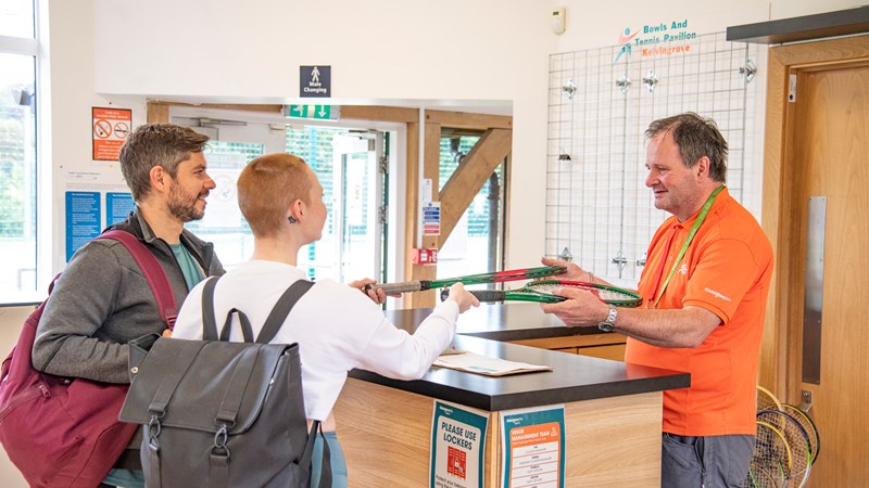 Two people collect tennis racquets from reception at Kelvingrove tennis courts. 