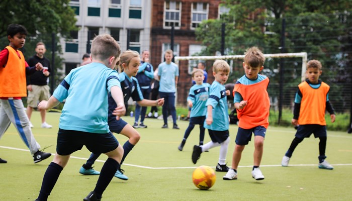 A group of young children, some with bibs over their strips, playing football in Glasgow