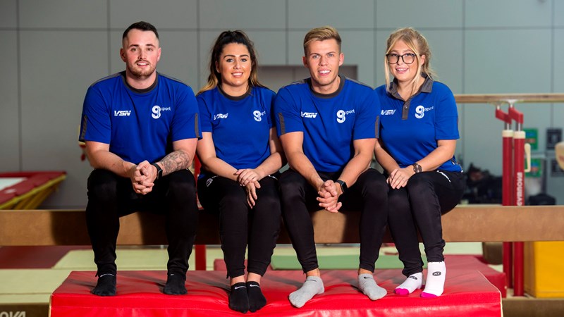 Four people sitting on a gymnastics balance beam