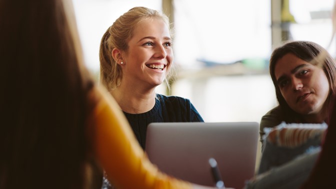 Group of young people sitting around a laptop smiling