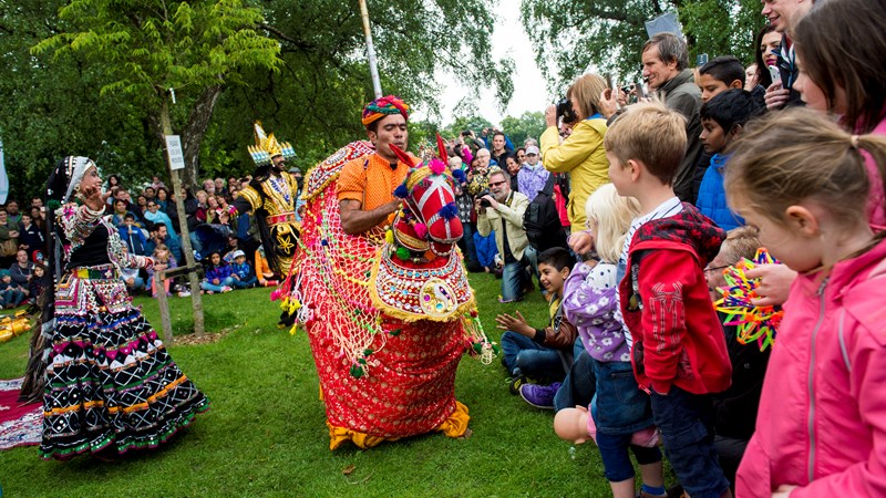 Children watching brightly coloured performers at Glasgow Mela with other members of the crowd taking photographs.