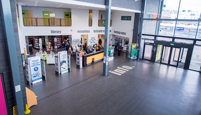 Large modern entrance to Pollok Library which has large windows, a grey floor with the word 'info' in white letters and a mezzanine