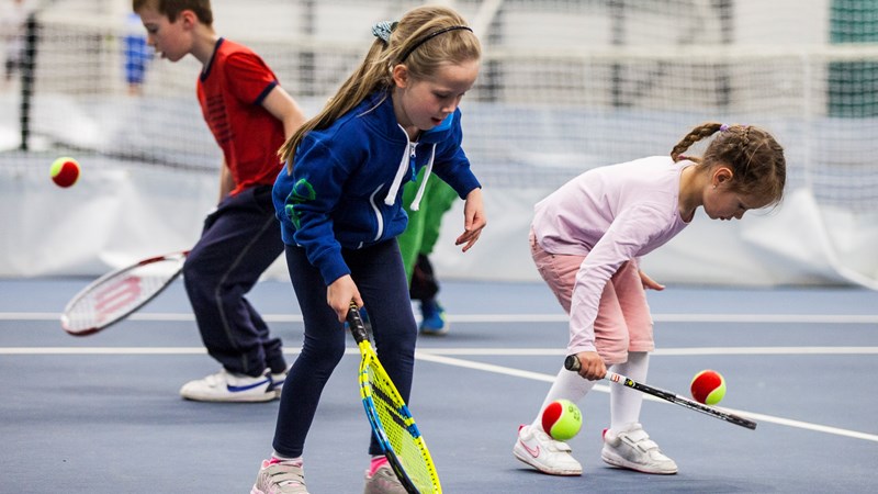 Children with rackets and balls playing tennis indoors