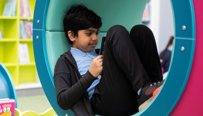 Primary aged child sitting reading a book, in a reading tunnel in the children's section of Woodside library