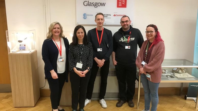 Five members of staff stand in a line in front of the BIPC Glasgow sign.