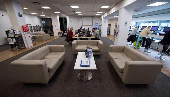 Annielsand Library main area. In the centre of this spacious room there are three sofas and a coffee table. Around the library you can see people using the PC's.