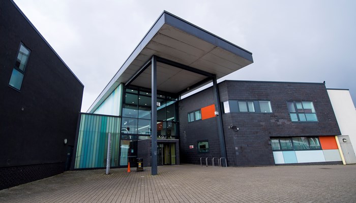 large, modern 2-storey building with a structural umbrella over the entrance. The building is grey and white.