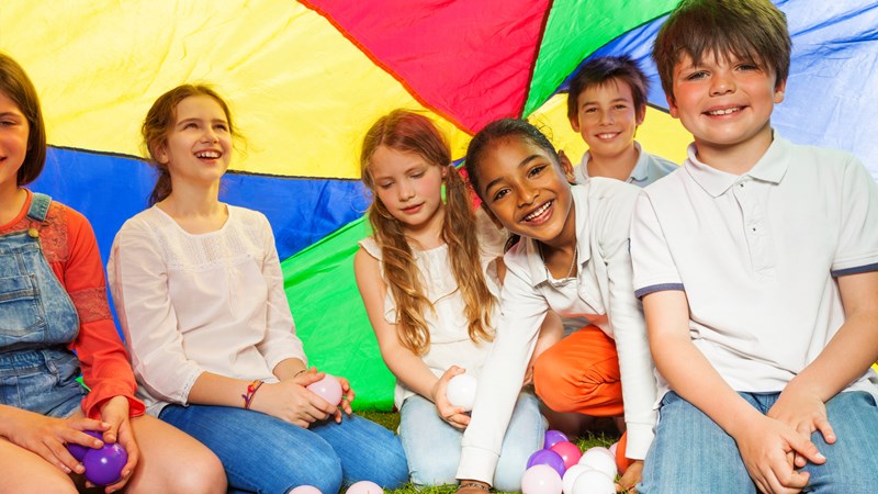 a group of children sitting on grass under a colourful tent