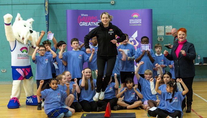 A group of children sitting and standing with their hands in the air alongside Scotland athletics start Eilidh Doyle.