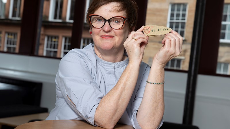 A smiling woman displays a small wooden artwork