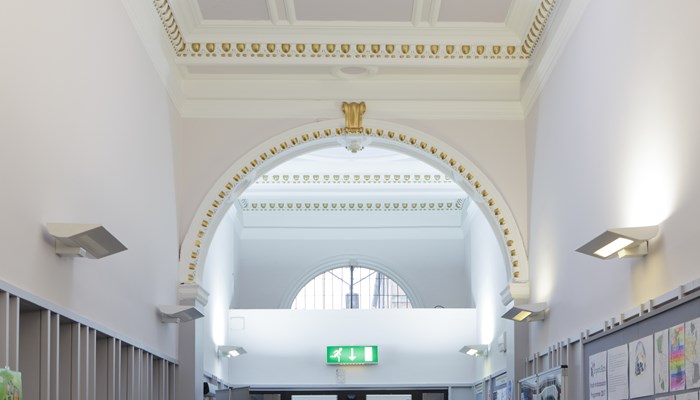 Hallway entrance before you reach the main library area. The ceilings are high and painted white with gold detail and there is an archway. On the walls to the right you can see colourful children's drawings. 