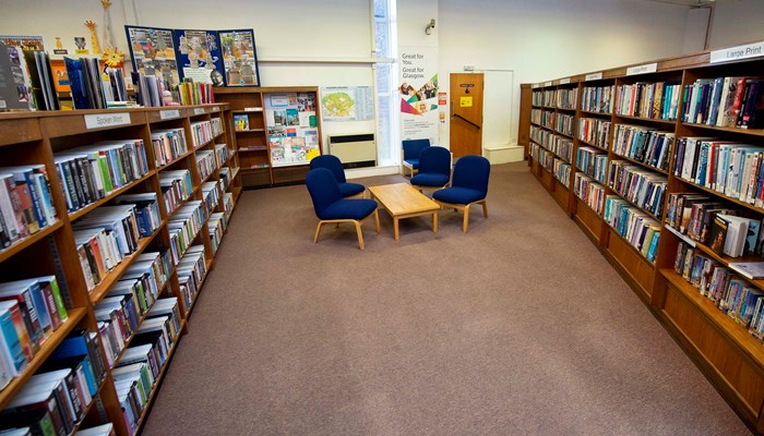 Two rows of wooden bookshelves at each side of the picture. In the middle is a coffee table with 4 blue soft chairs