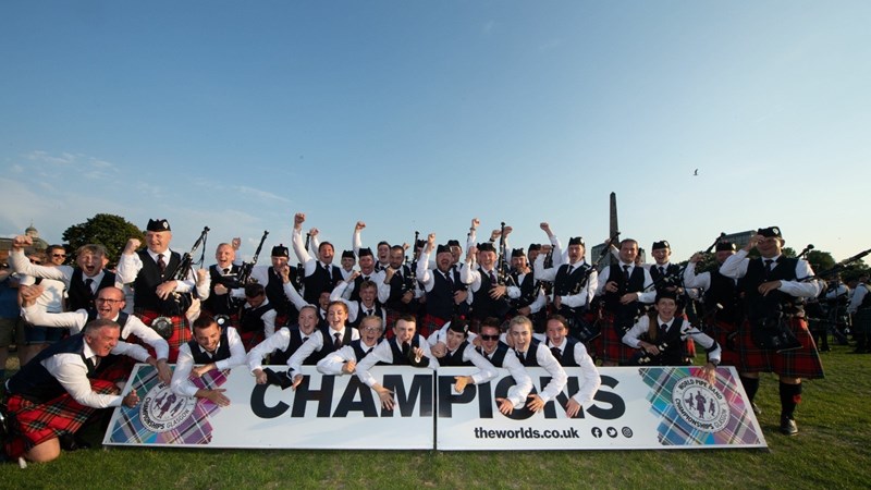 Pipers and drummers in pipe band uniforms celebrate in sunny weather on a Glasgow Park