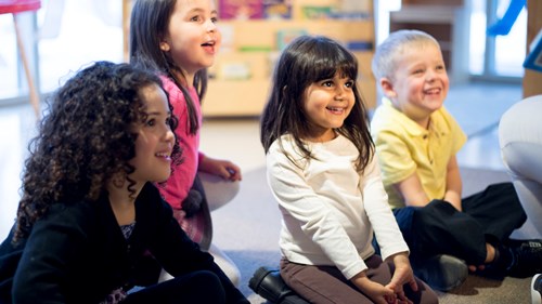 Group of children in a library smiling and listening to someone reading a story