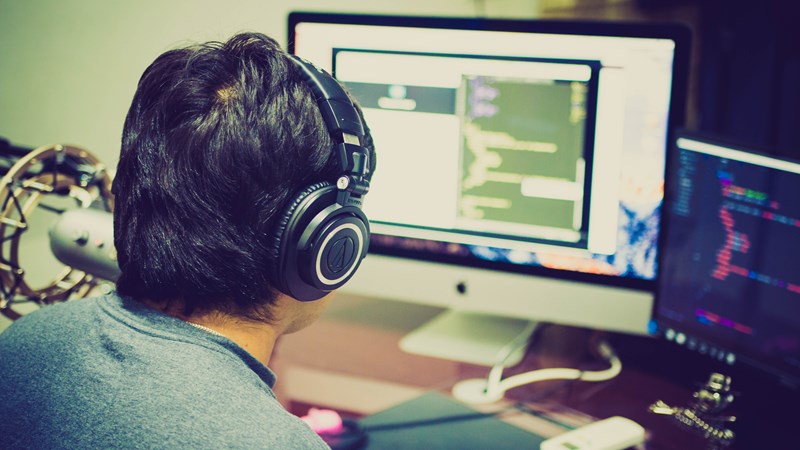 Close up of the back of a persons head facing a large computer monitor and a smaller computer monitor